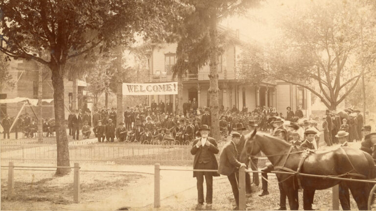 Crowds of people, house in background, "Welcome!" banner posted